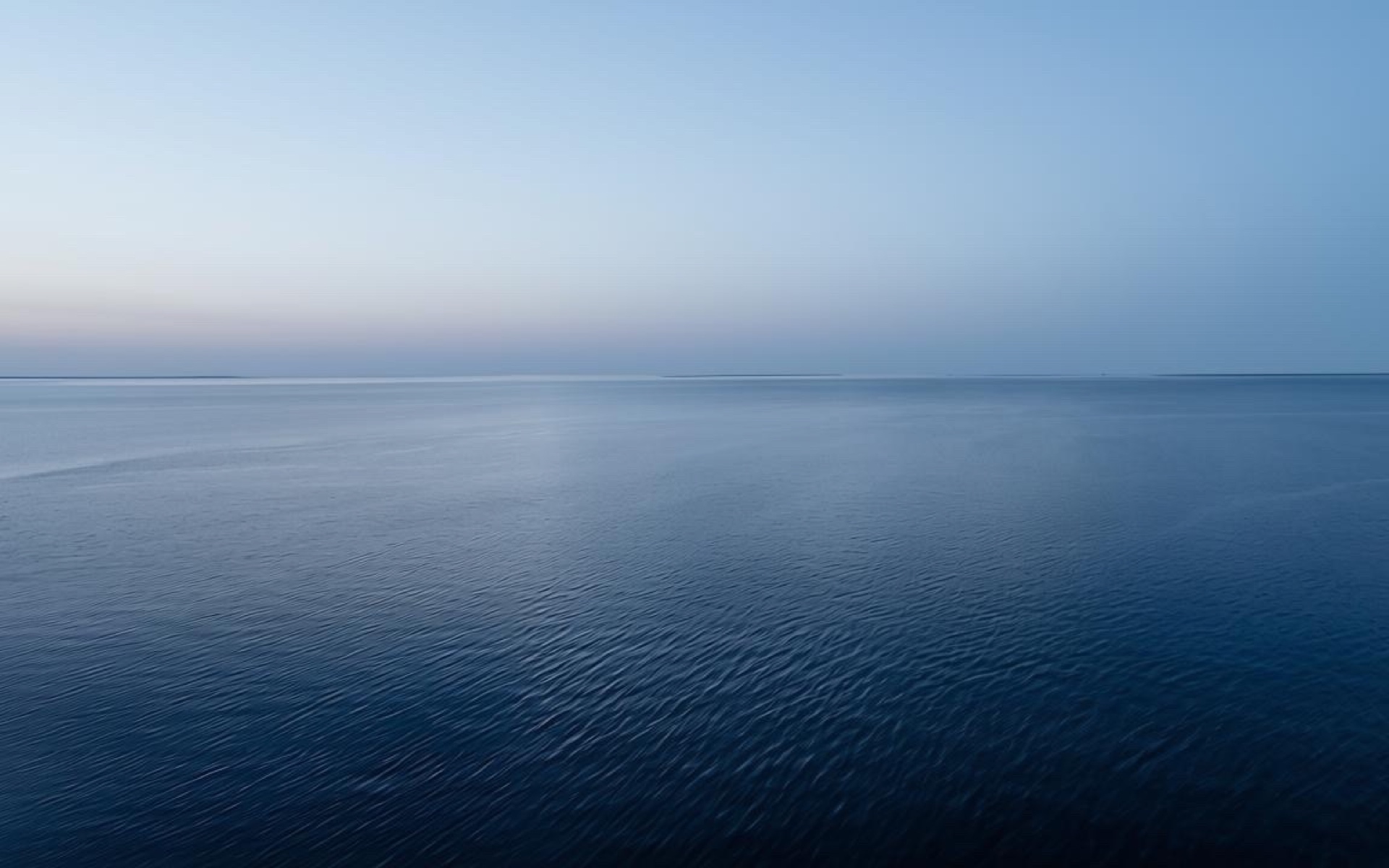 Ruhige dunkelblaue Meer­esfläche mit leichter Wellenstruktur, heller Horizont im oberen Bilddrittel