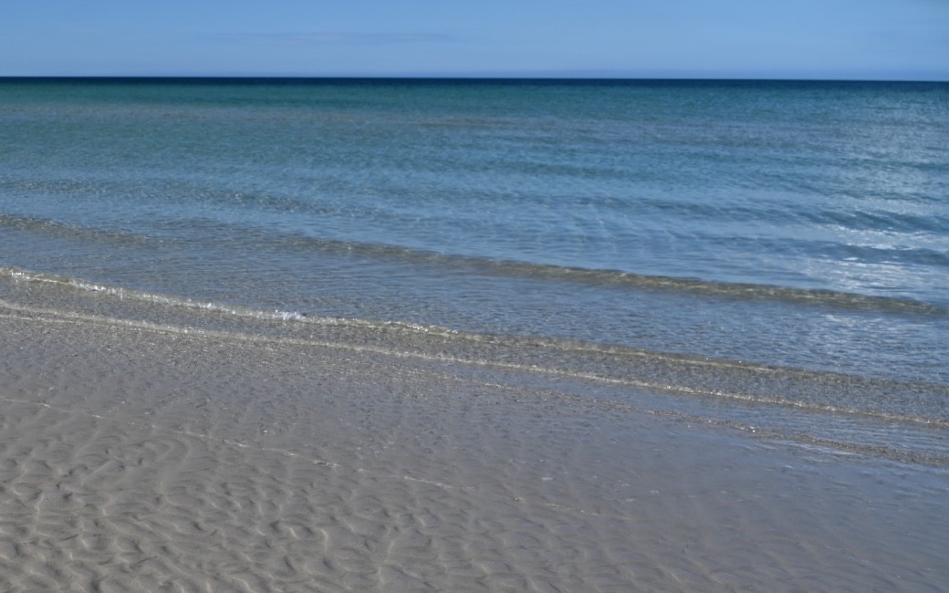 Wellenlinie an einem Strand, wo Wasser sanft auf nassen Sand läuft, weiche Übergänge – Symbolbild für fließende Übergänge zwischen Coaching und Psychotherapie
